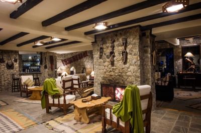 Cozy lounge with stone walls, wooden beams, a fireplace, and rustic furniture at The Dwarika’s Hotels and Resorts