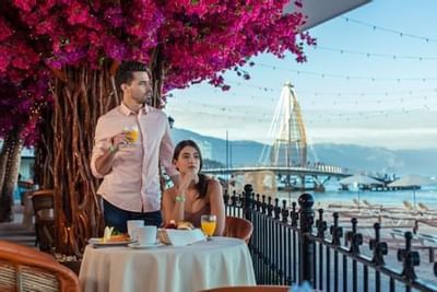 Couple enjoying beachfront dining under vibrant bougainvillea tree with ocean views at Playa Los Arcos Puerto Vallarta