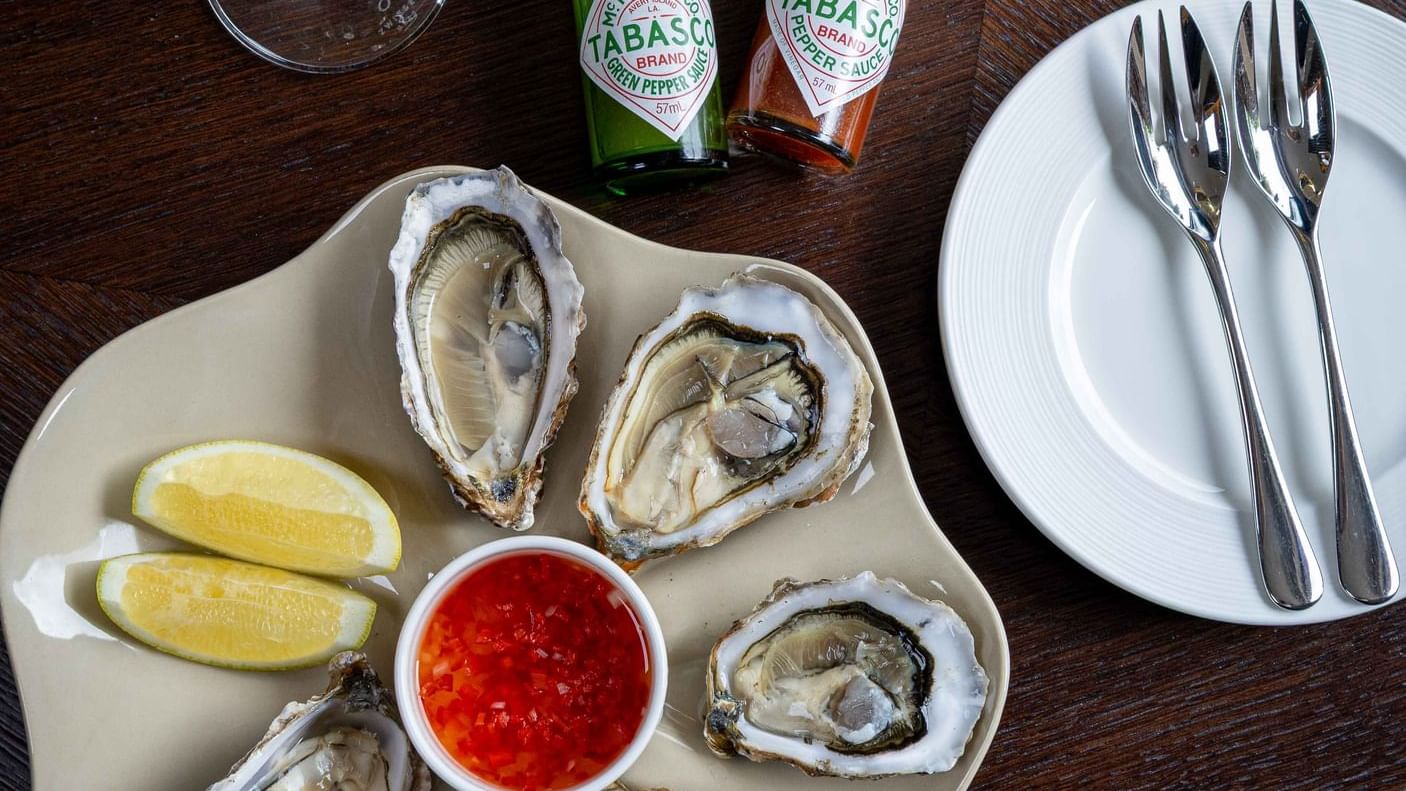 Platter of fresh oysters with lemon wedges and a red sauce, served on a table at Seaton House