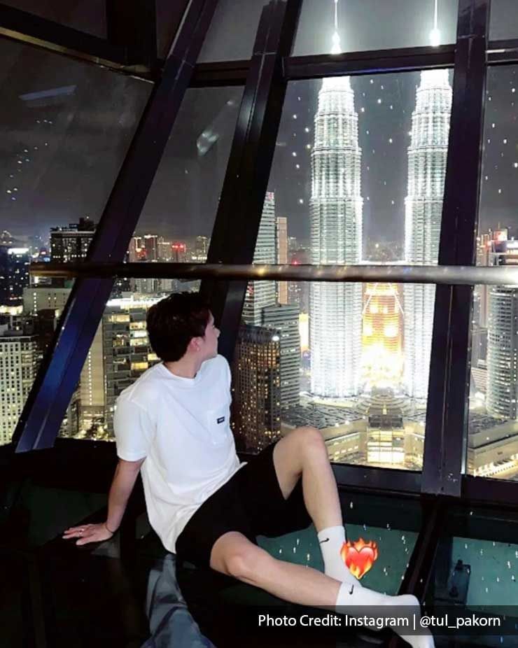 A man seated on the floor of the Sky Deck at Imperial Lexis Kuala Lumpur, enjoying a view of the Petronas Twin Towers.