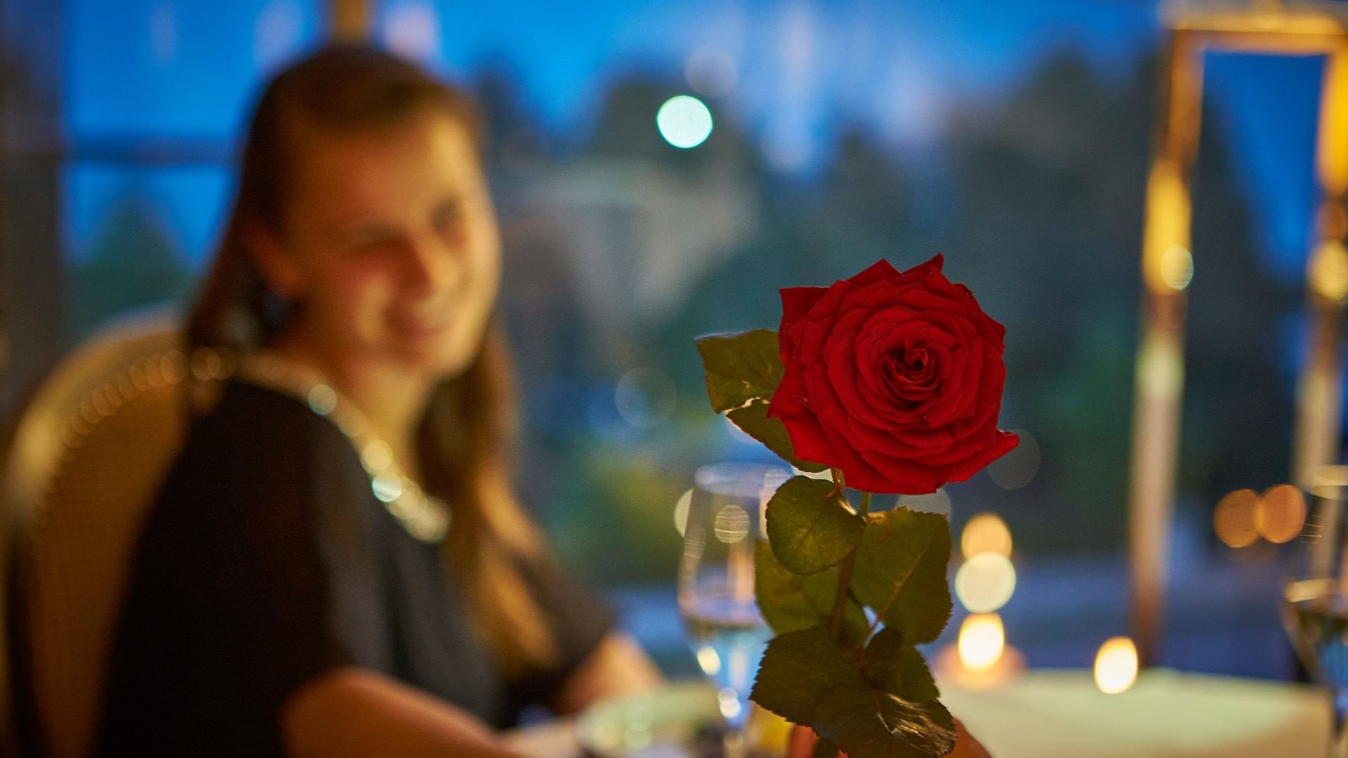 Woman smiling with red rose and wine glass in foreground at Falkensteiner Schlosshotel Velden