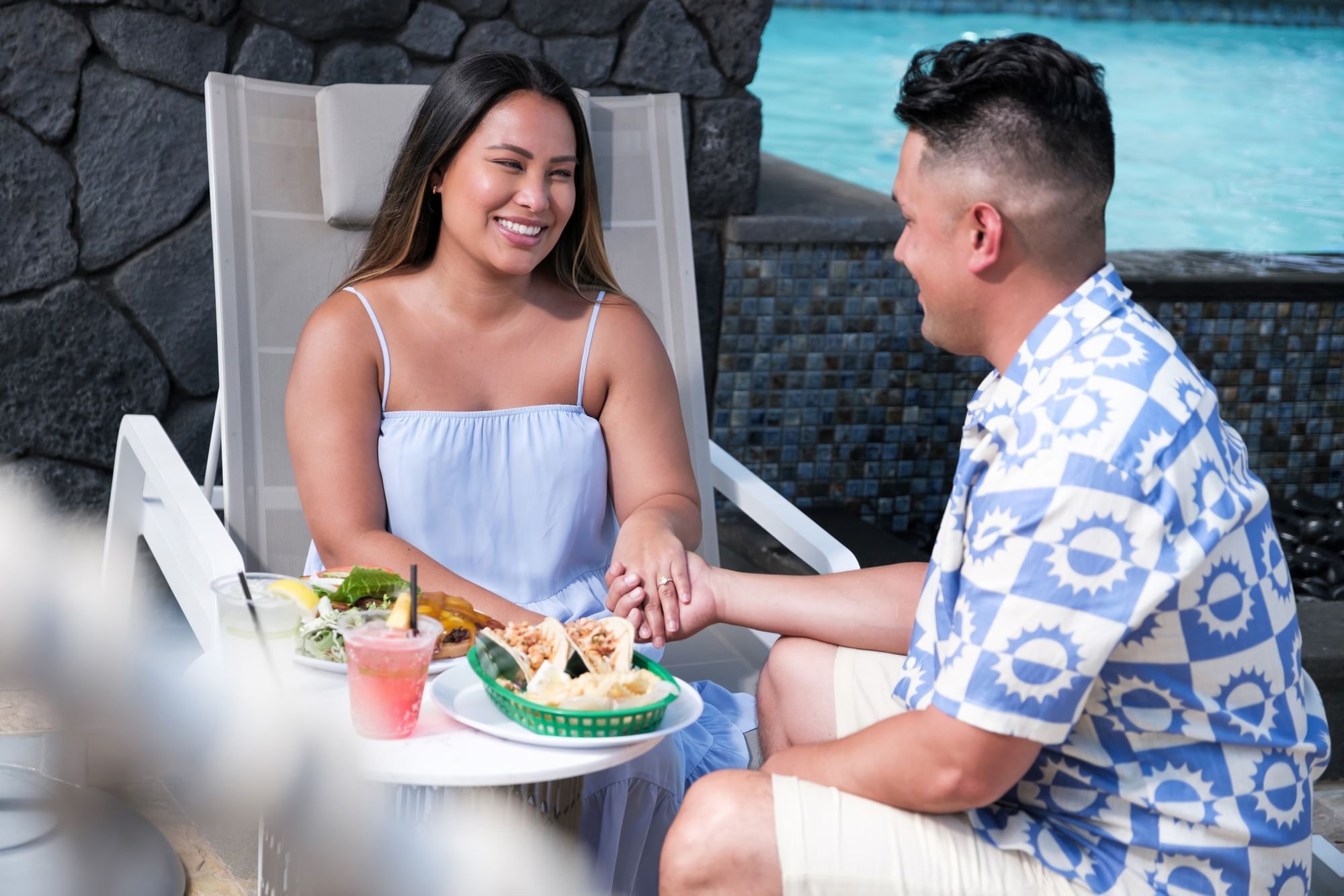 A couple enjoys a meal and drinks by the pool.