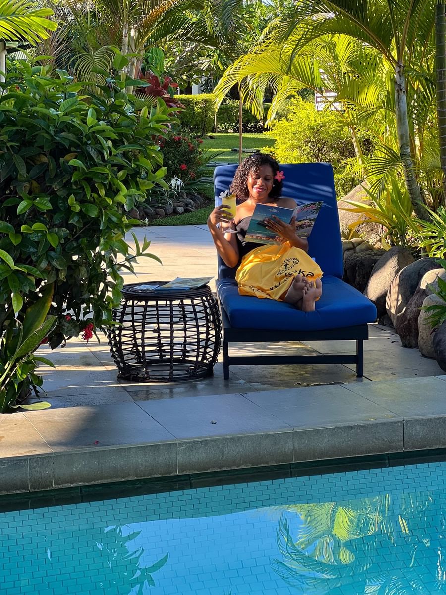 Guest enjoying a drink on a blue lounger by a wicker table near lush plants at TokaToka Resort Nadi Fiji