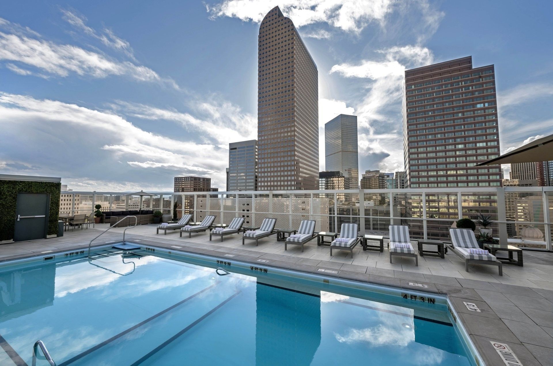 Rooftop pool with loungers by a glass fence under a sky with city buildings at Warwick Denver