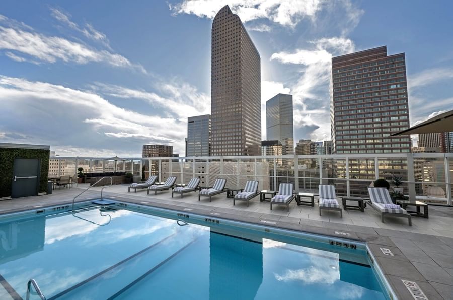Rooftop pool with loungers by a glass fence under a sky with city buildings at Warwick Denver