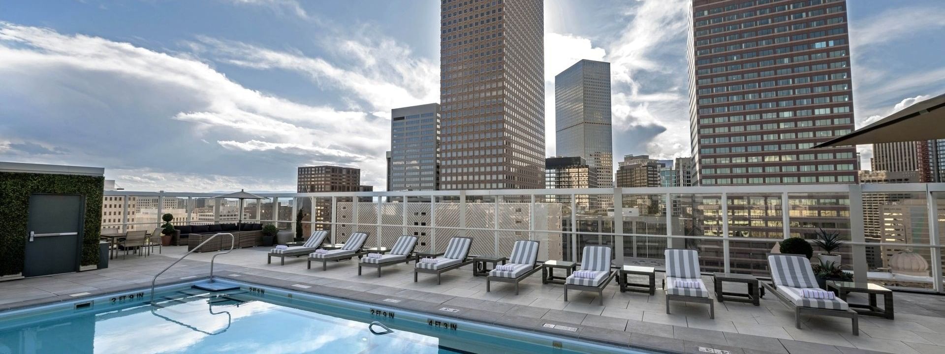 Rooftop pool with loungers by a glass fence under a sky with city buildings at Warwick Denver