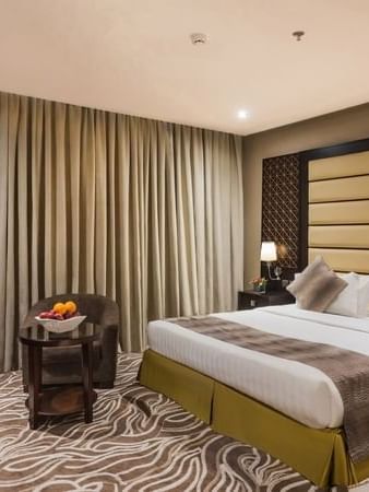 Fruit bowl on a table by an chair under heavy drapes near the bed in Deluxe King / Twin Room at Naviti by Warwick Al Khobar