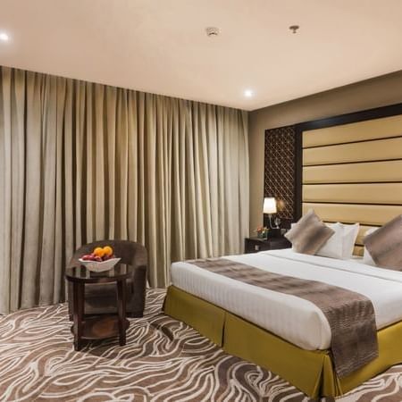 Fruit bowl on a table by an chair under heavy drapes near the bed in Deluxe King / Twin Room at Naviti by Warwick Al Khobar