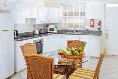 Kitchen with white cabinetry, granite countertops, and a dining table in Two Bedroom Croton Suite at Bay Gardens Hotel