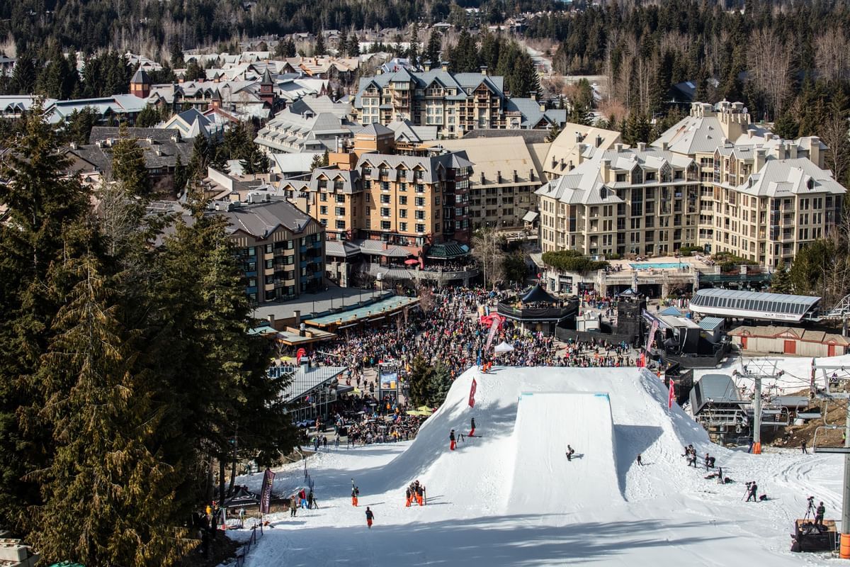 Snowboarder gliding down a slope in front of large crowd of people near Blackcomb Springs Suites