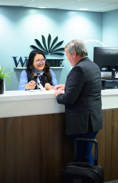 Friendly front desk agent assisting a male guest at the registration counter check-in area of Rodd Moncton