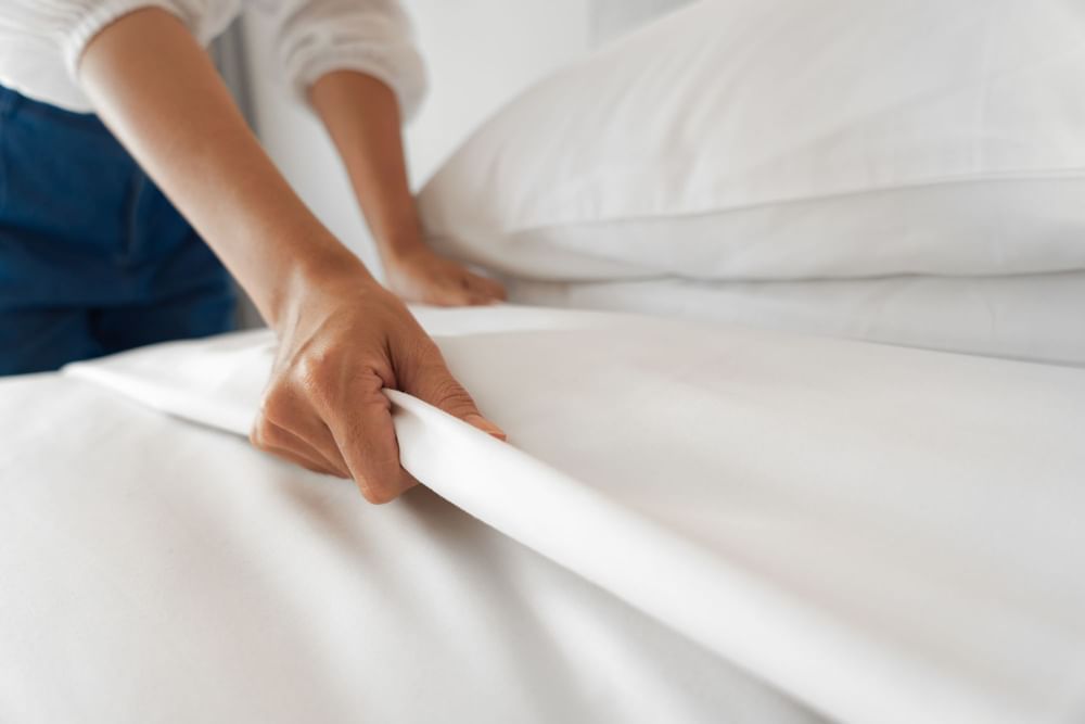 woman making bed with white sheets in hotel