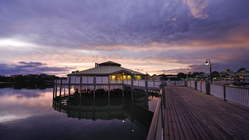 Wooden pier extends toward Lily’s on the Lagoon, reflecting a colorful sunset at Novotel Sunshine Coast Resort