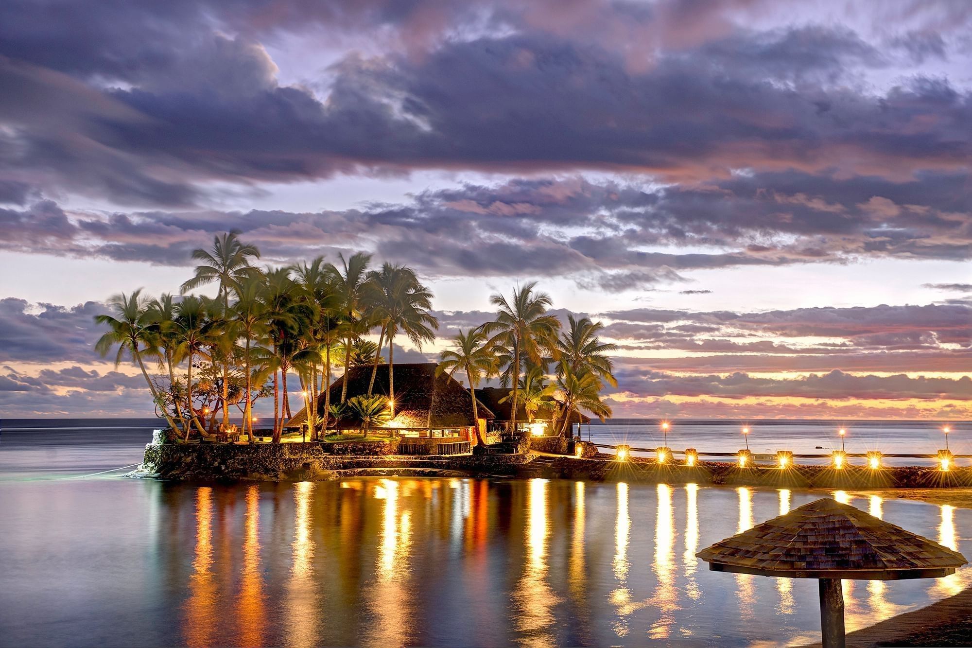 Island restaurant by a calm sea under a purple sunset near glowing pier lights at Warwick Fiji Resort and Spa