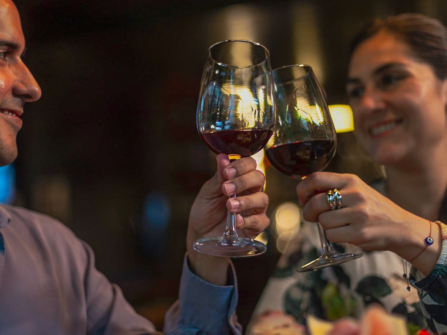 Couple toasting with red wine glasses in a dimly lit setting at El Silencio Lodge and Spa