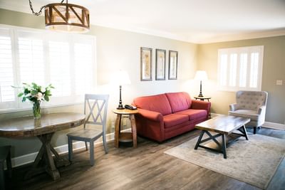 Living room with red sofa, wooden coffee table, rug, armchair, round dining table, and a window with shutters.