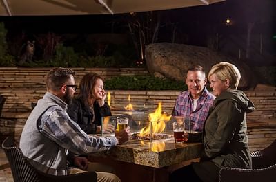 A group of friends enjoys drinks and conversation around a warm fire pit at The Stanley Hotel, on a pleasant evening