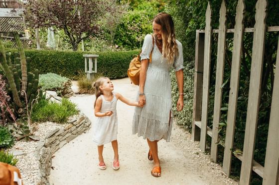 Woman & young girl holding hands walking through garden pathway at Cambria Pines Lodge, one of the top hotels in Cambria, CA