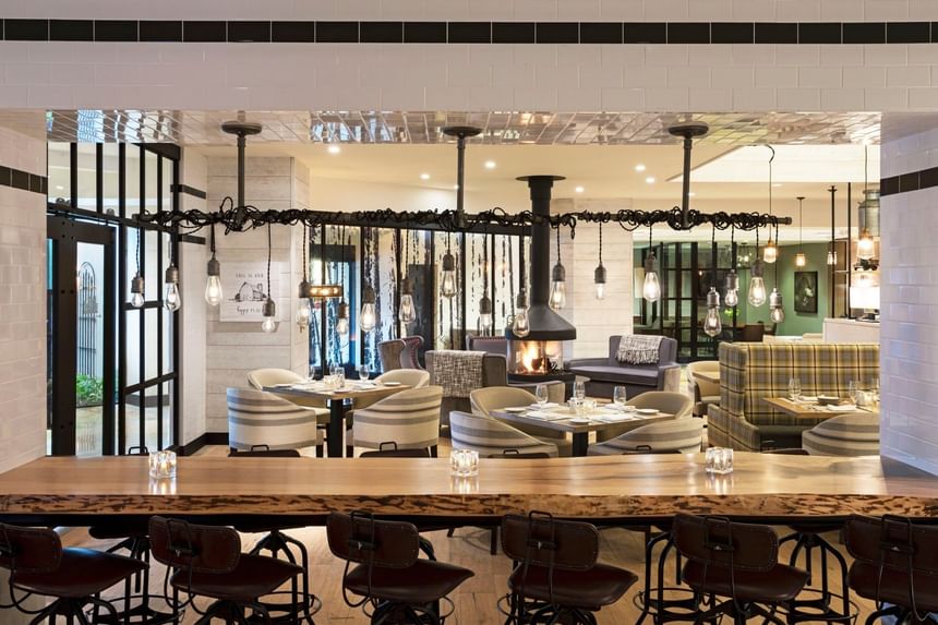 Seating with hanging bulb lights and a center fireplace in Farmhouse Social Kitchen & Bar at Sable Oaks Weddings and Events