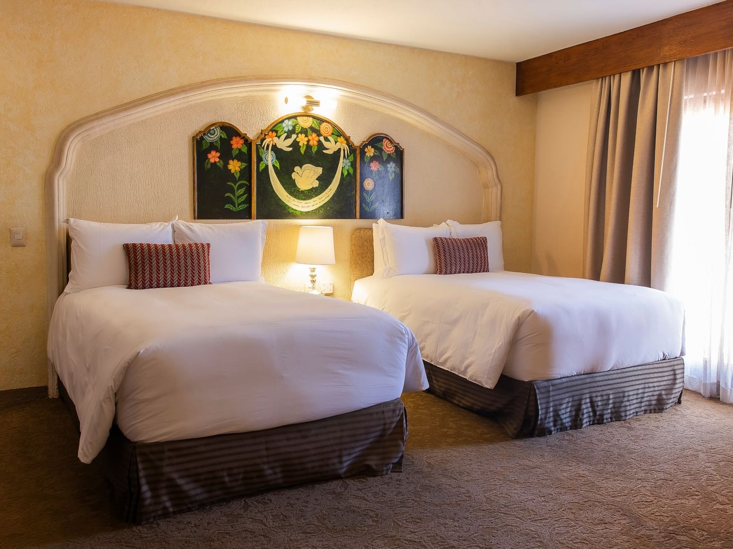 Two double beds with white linens and decorative headboard featuring colonial artwork at Quinta Real Zacatecas