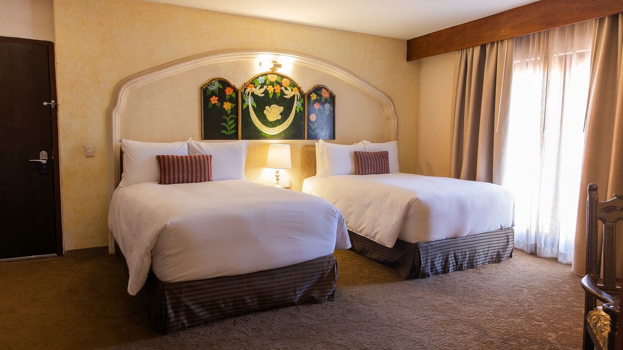 Two double beds with white linens and decorative headboard featuring colonial artwork at Quinta Real Zacatecas