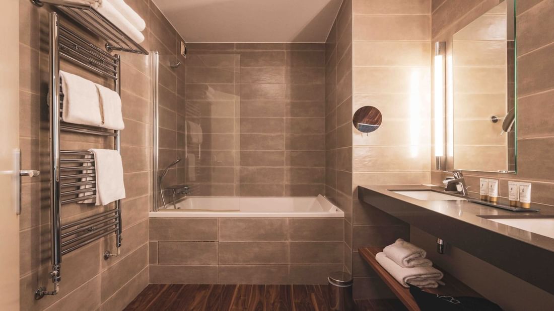 Bathroom with bathtub, two sinks, and towel racks, featuring wooden floors and tiled walls.