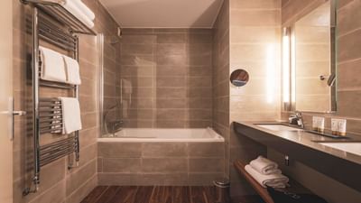 Modern bathroom with tiled walls, wooden floor, two sinks, bathtub, and towels.