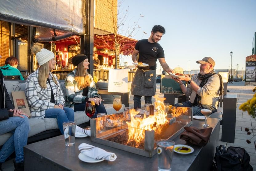 Friends toasting beer by a fireplace in Tuscan Market at The Artisan Hotel at Tuscan Village