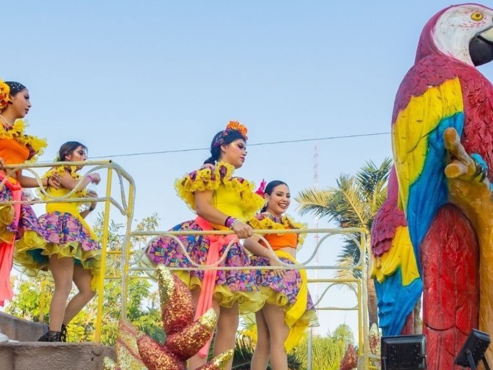 Artistas con vestidos coloridos sobre una carroza de desfile cerca de Camino Real Hotels