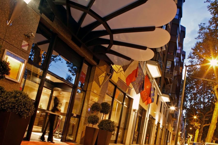 Street view of the modern Warwick Reine Astrid - Lyon entrance at dusk with a canopy, flags, and glass doors