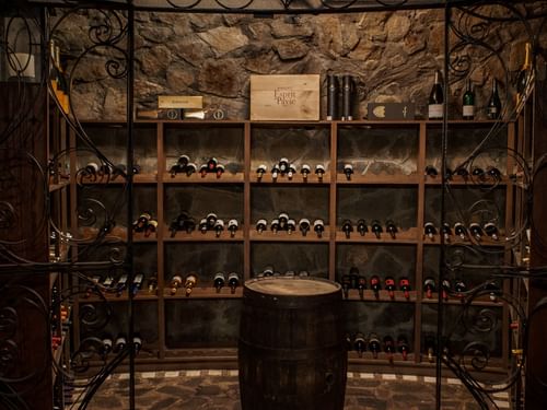 Cozy wine cellar with stone walls, a leather chair, and bottles of wine at La Cava de Santiago in Hacienda del Mar Los Cabos.