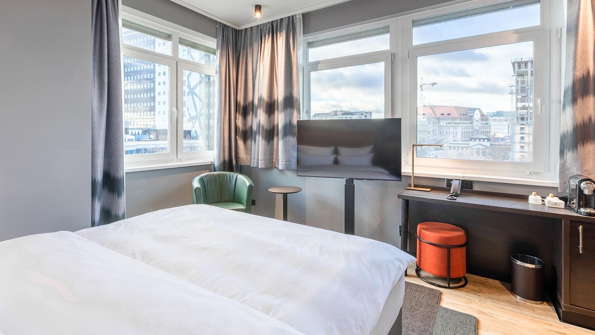 Ein großes Bett mit einem Fenster mit Blick auf die Stadt im Superior Zimmer des Titanic Comfort Kurfürstendamm
