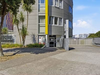 Modern curved building with entrance and parking at Student Living Auckland - Beach.