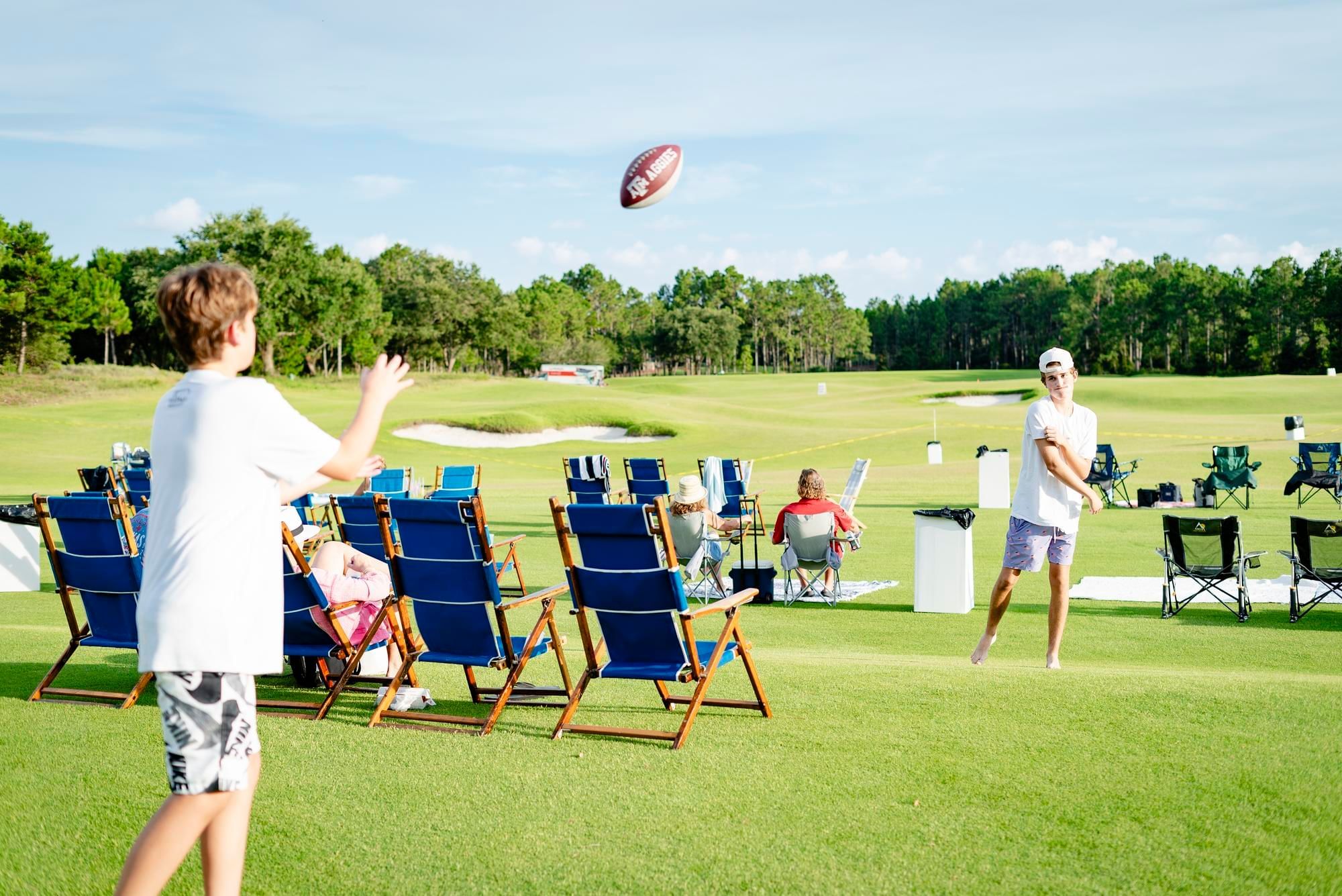 Two boys throwing a football back and forth while waiting for the fireworks show on the Camp Creek driving range