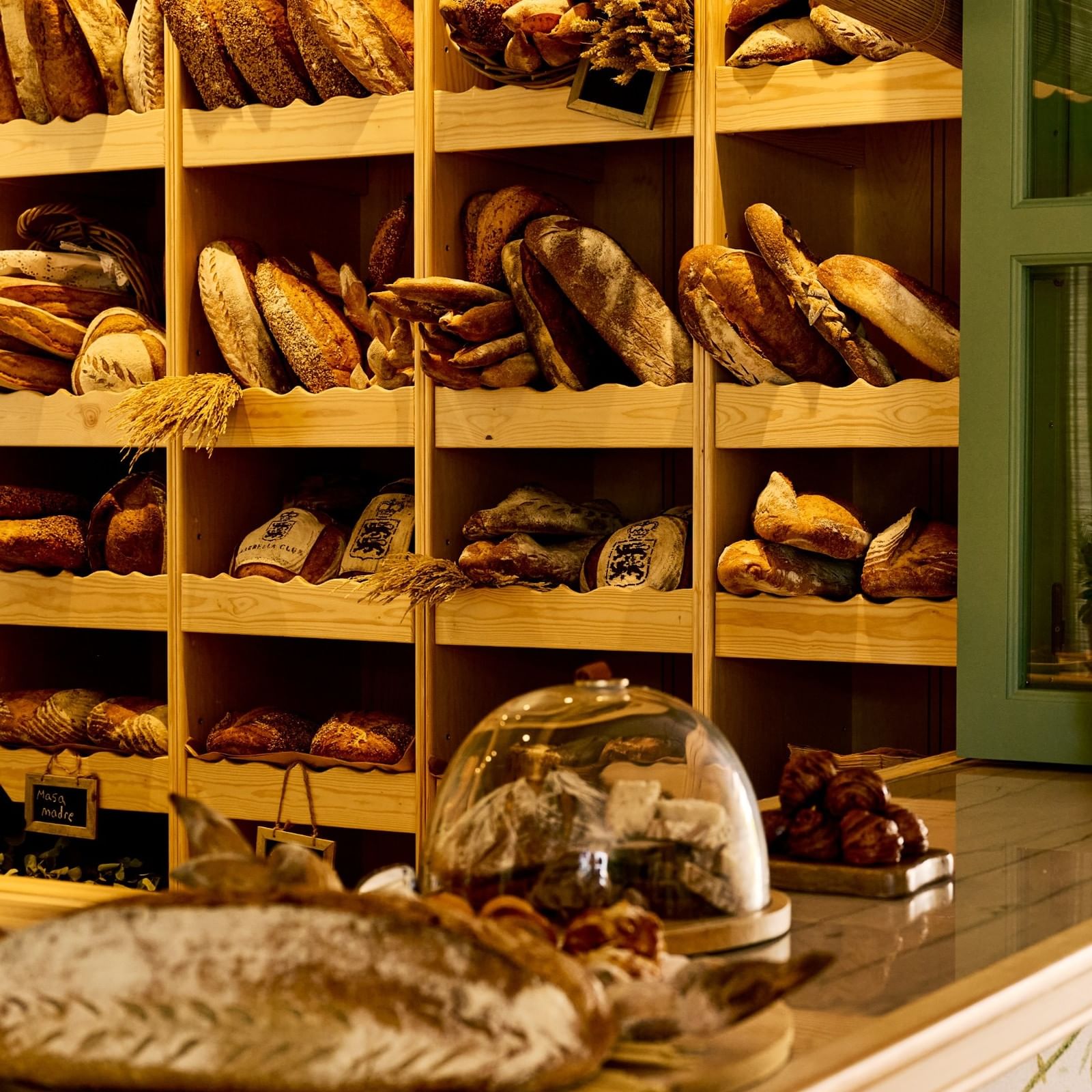 Wooden shelves displaying artisan breads and pastries with a rustic counter at El Obrador at Marbella Club