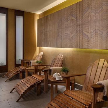 Wooden lounge chairs with tables, teapot, and plants in the resting area of Titanic City Taksim's spa.
