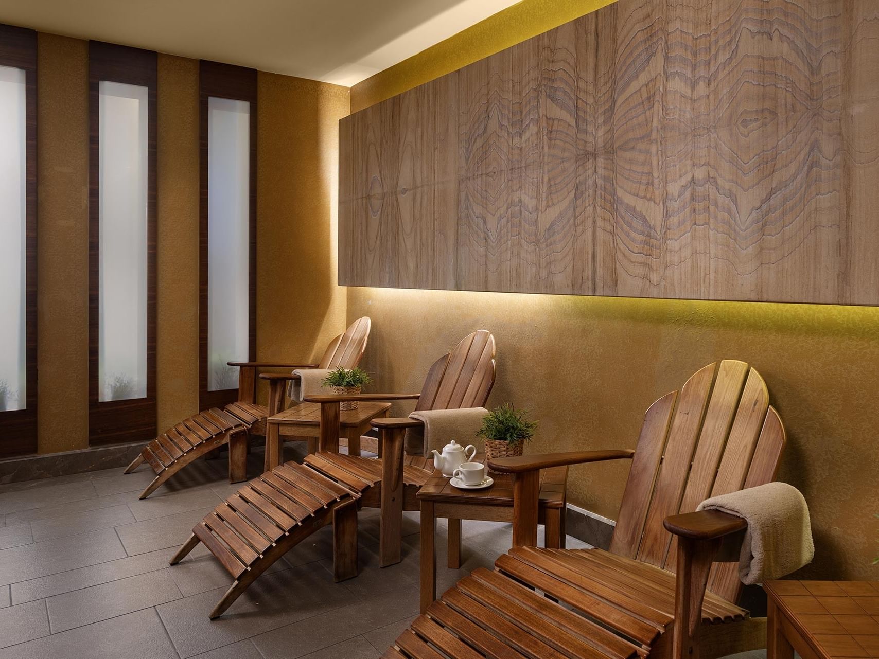 Wooden lounge chairs with tables, teapot, and plants in the resting area of Titanic City Taksim's spa.