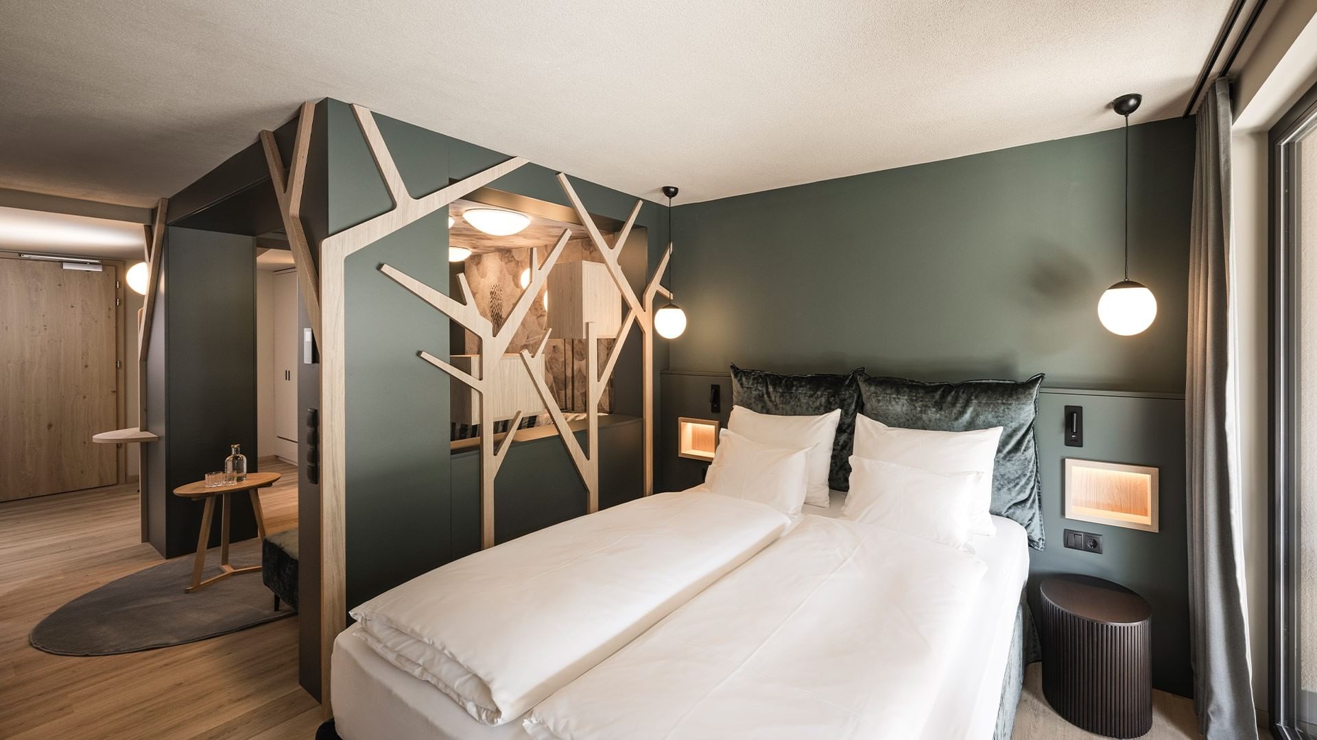 Hotelzimmer mit zwei Betten, Holzfußboden, grauen Wänden und einer Trennwand mit Baumdesign.