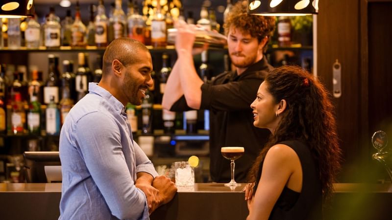 Couple chatting at the bar while a bartender mixes a drink at Eat Street.