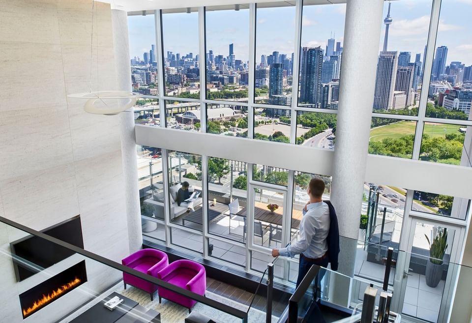 Homme regardant le paysage urbain à travers de grandes fenêtres dans la suite Penthouse de l'hôtel X Toronto
