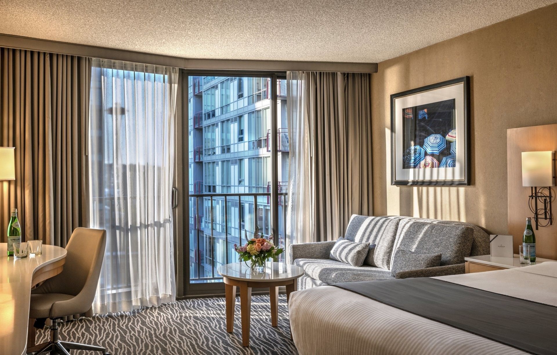 A wide view of a hotel room with a desk, sofa, bed, and city view.