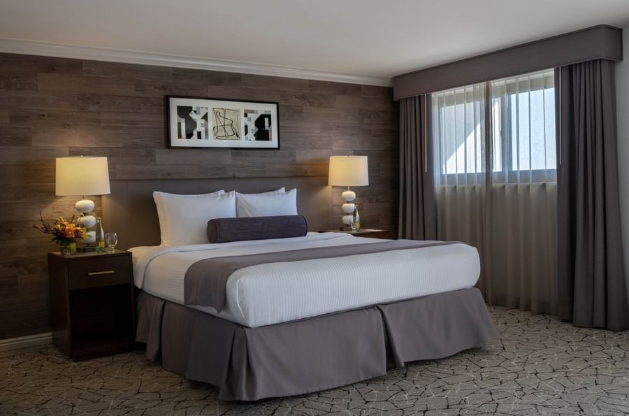 King bed by white lamps on dark nightstands under a decorative wood-slat wall in Premier Junior Suite at Warwick Denver