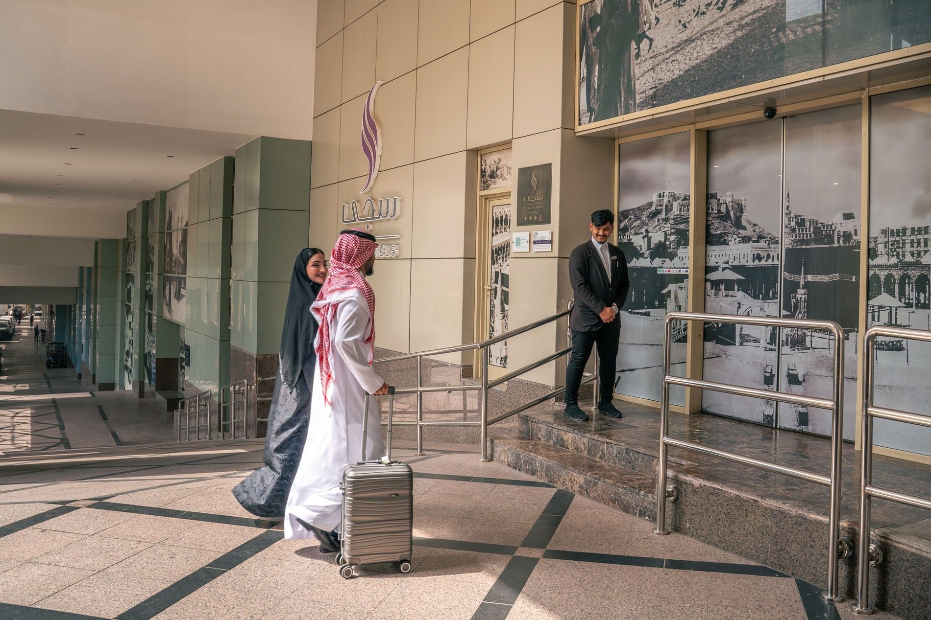 Couple with luggage walking through the hotel entrance with a doorman at Saja by Warwick Makkah