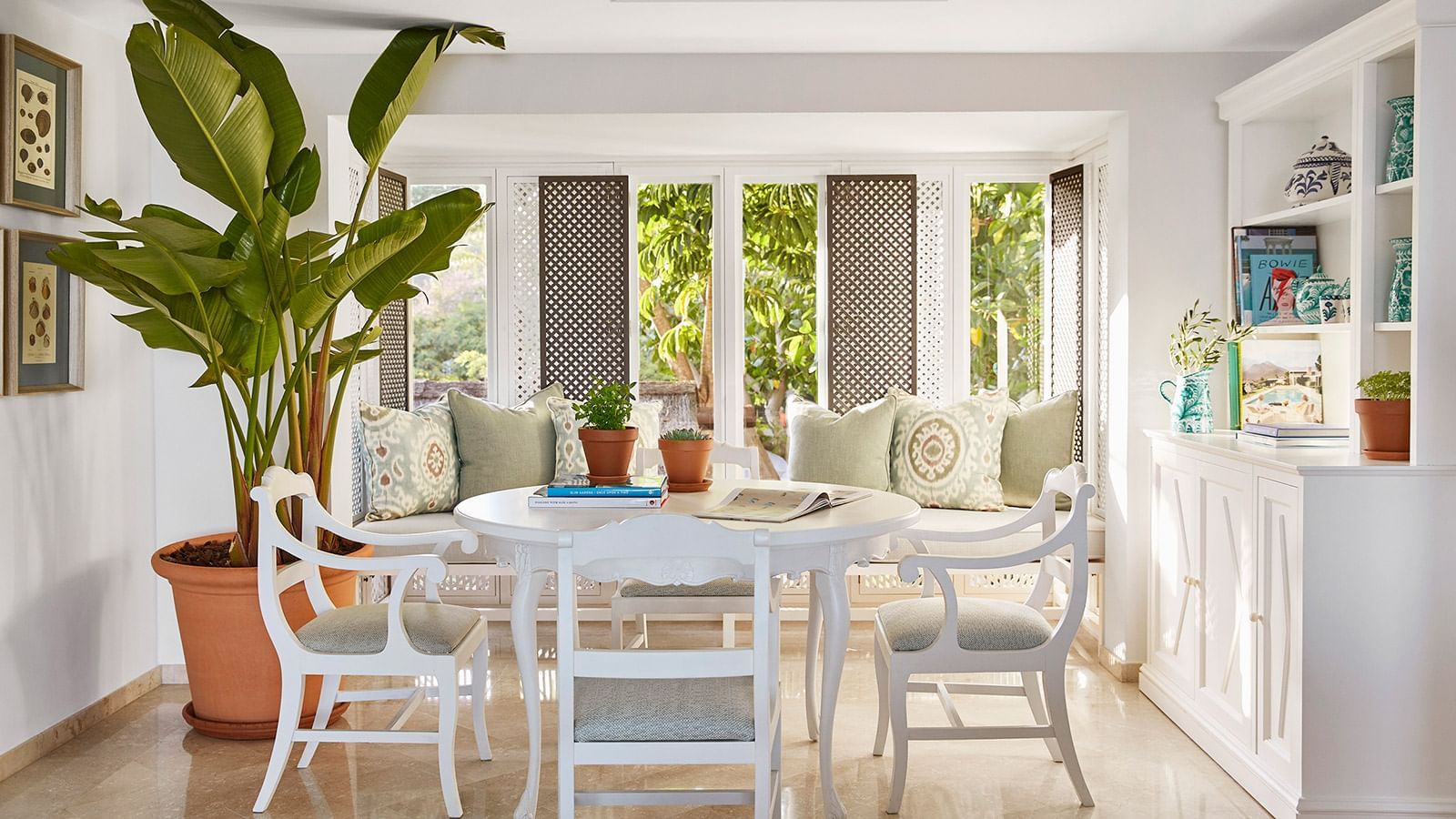 Royal Beach Suite dining nook with window seat, lattice screens, white chairs, and plants at Marbella Club