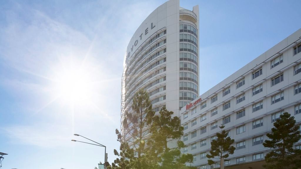 Novotel Sydney Olympic Park with a curved facade and surrounding palm trees under a bright sky