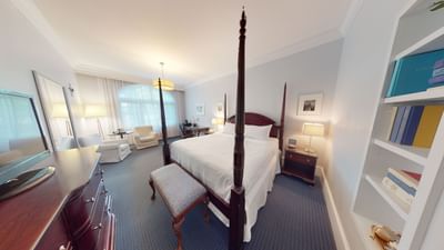 Four-poster bed with bench beside nightstand with table lamp near armchairs in Luxury guest room at Avon Old Farms Hotel