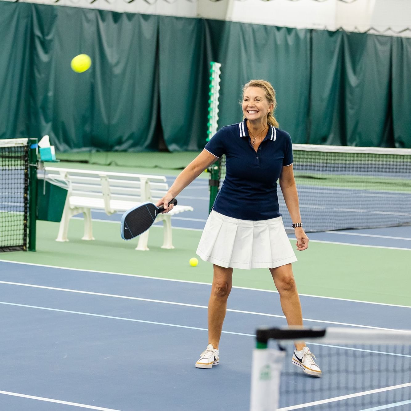 Woman smiling and playing pickleball on a tennis court during Coed Beginner to Intermediate Pickleball Open Play.
