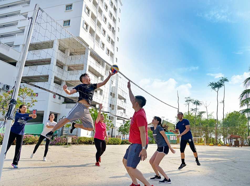 Group playing volleyball in a city park with buildings and trees in the background - Lexis Port Dickson