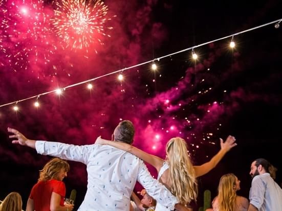 Pareja bailando entre invitados con fuegos artificiales de Año Nuevo.