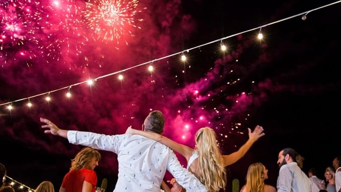 Pareja bailando entre invitados con fuegos artificiales de Año Nuevo.
